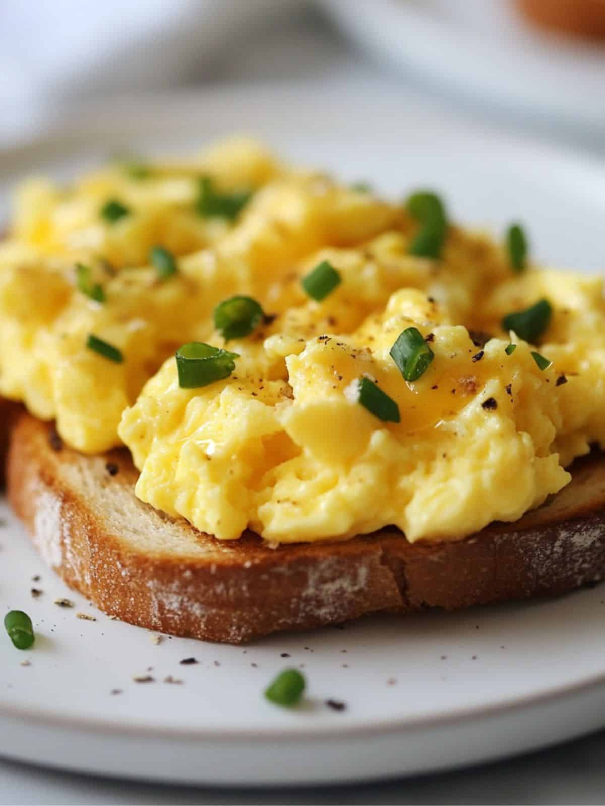 A close up image of scrambled eggs on toast topped with chives and on a white plate.