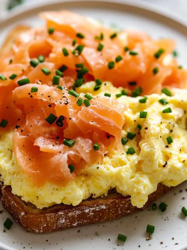 A close up image of scrambled eggs and smoked salmon on toast. Topped with chives and on a white plate.