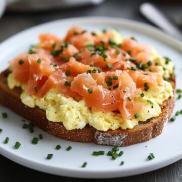 Scrambled eggs and smoked salmon on toast placed on a white plate and scattered with chopped chives.