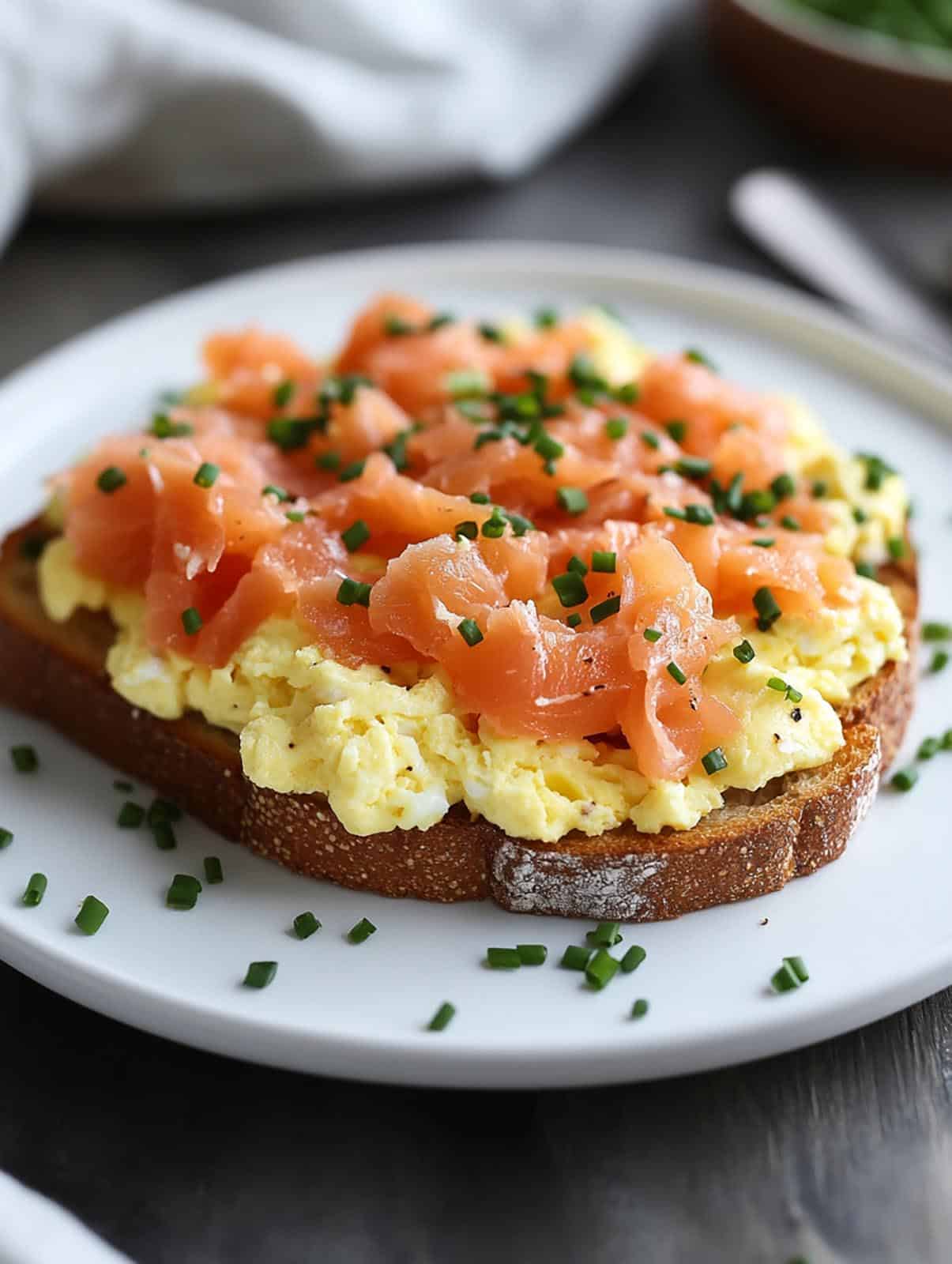 Scrambled eggs and smoked salmon on toast placed on a white plate and scattered with chopped chives.