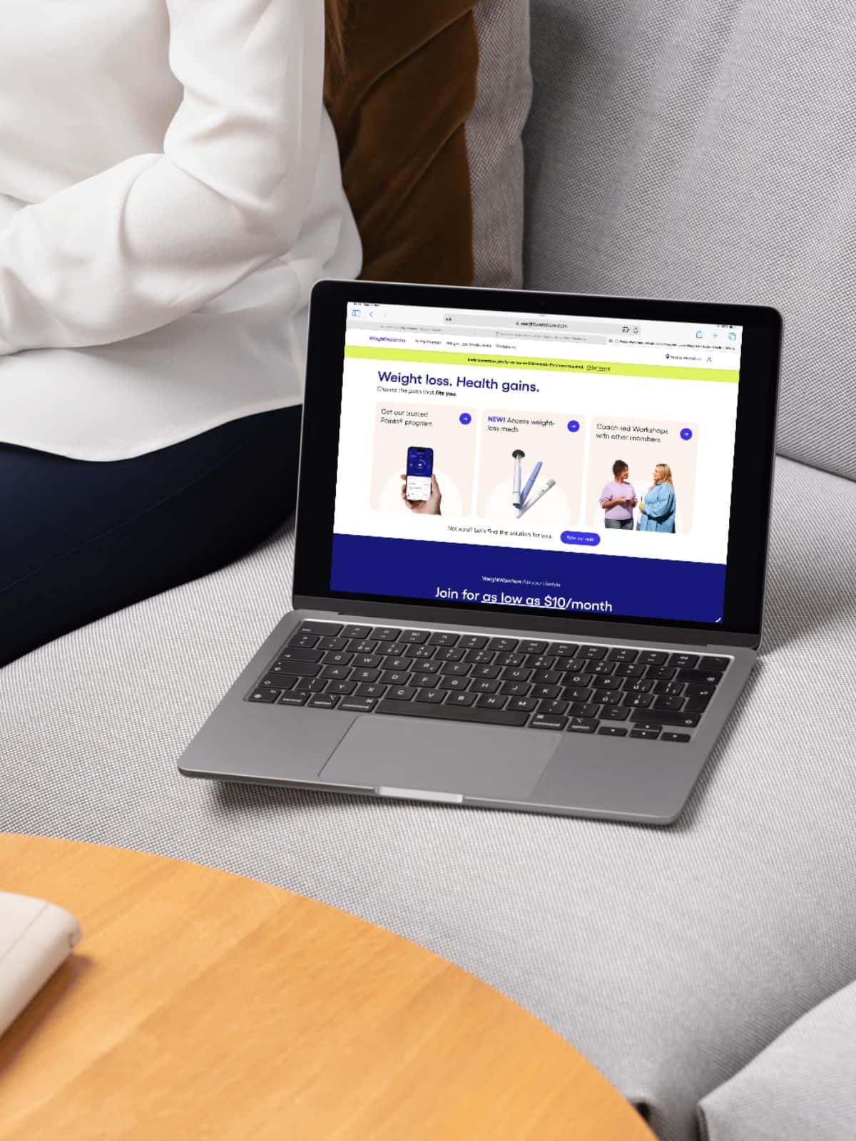 A laptop open on a sofa next to a person. On the screen is the sign up page for weight watchers.