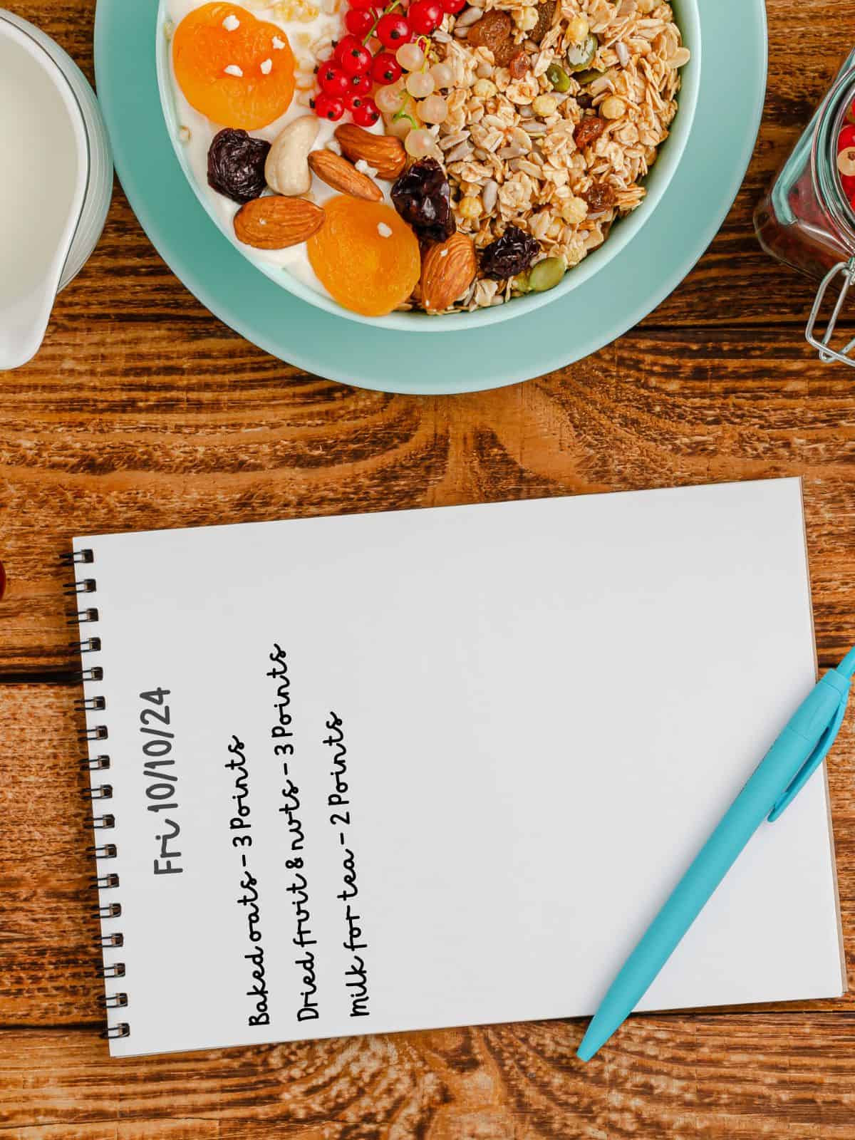 A food diary on a wooden table next to a blue bowl full of muesli.